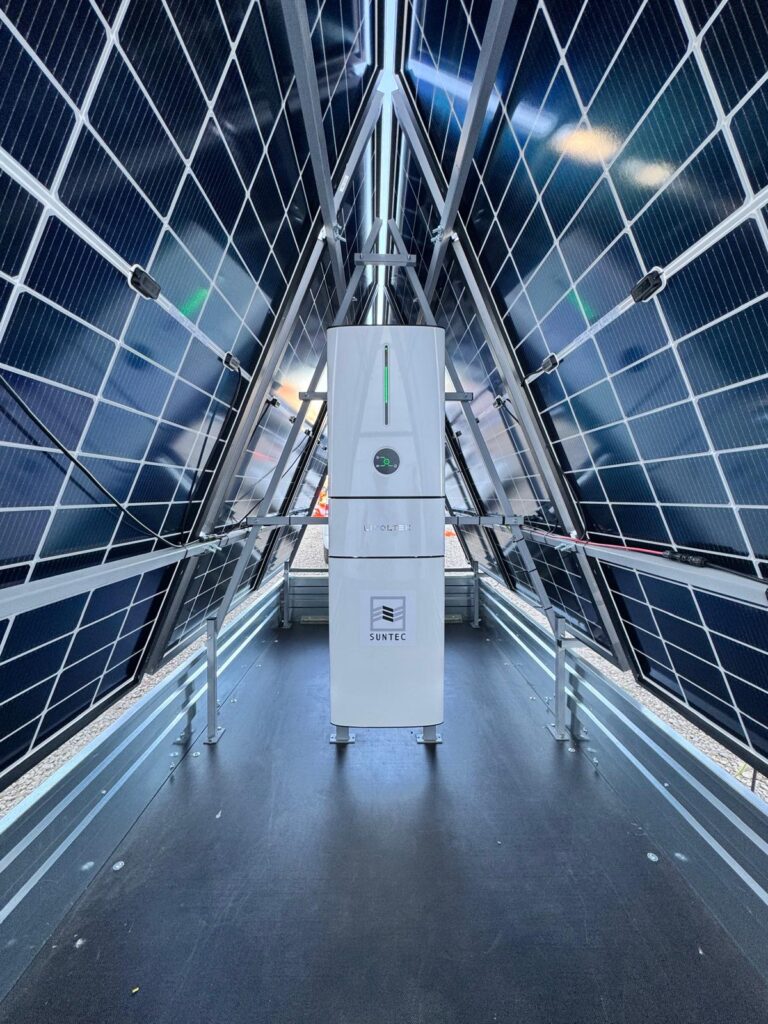 PHOTO-2025-07-01-19-54-22 3 - Suntec Central white solar inverter cabinet labeled SUNTEC surrounded by a tunnel of blue solar panels.